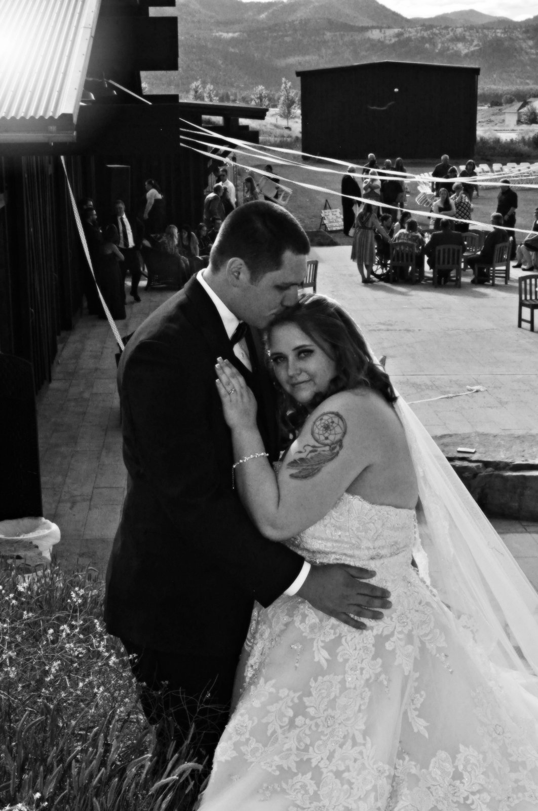 Couple embrace on the patio as reception guests gather
